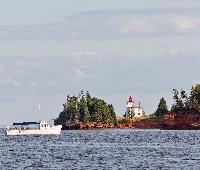 A lighthouse at the mouth of the Charlottetown harbour sits while a boat cruise passes nearby
